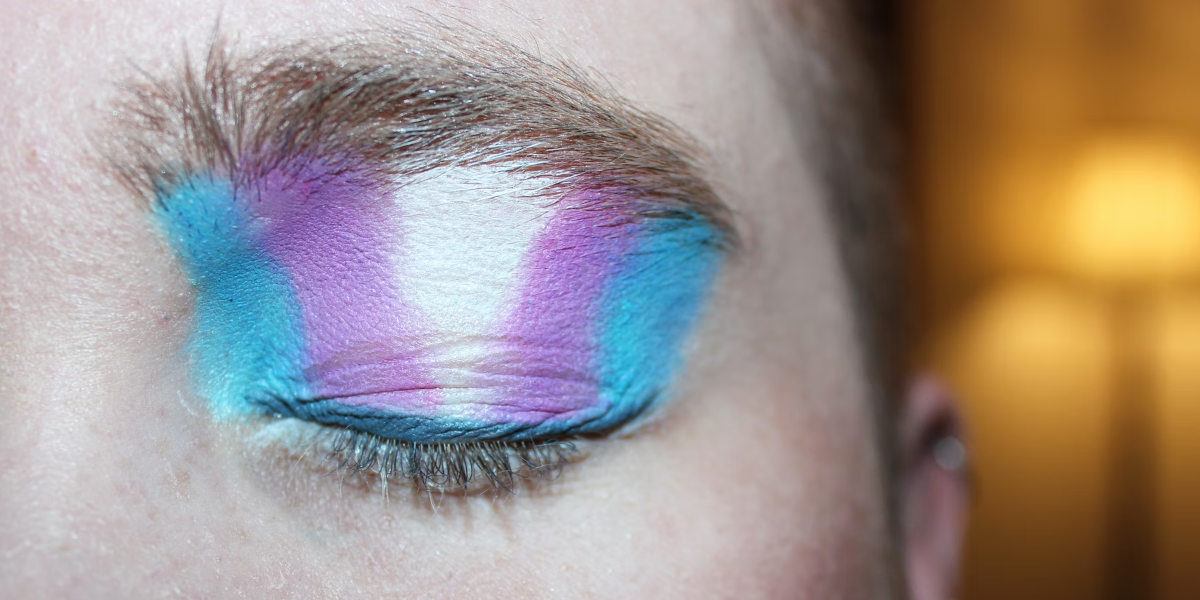 A closeup of a closed eye with eyeshadow in the colours of trans flag (https://unsplash.com/photos/a0KL1Um0wBA)