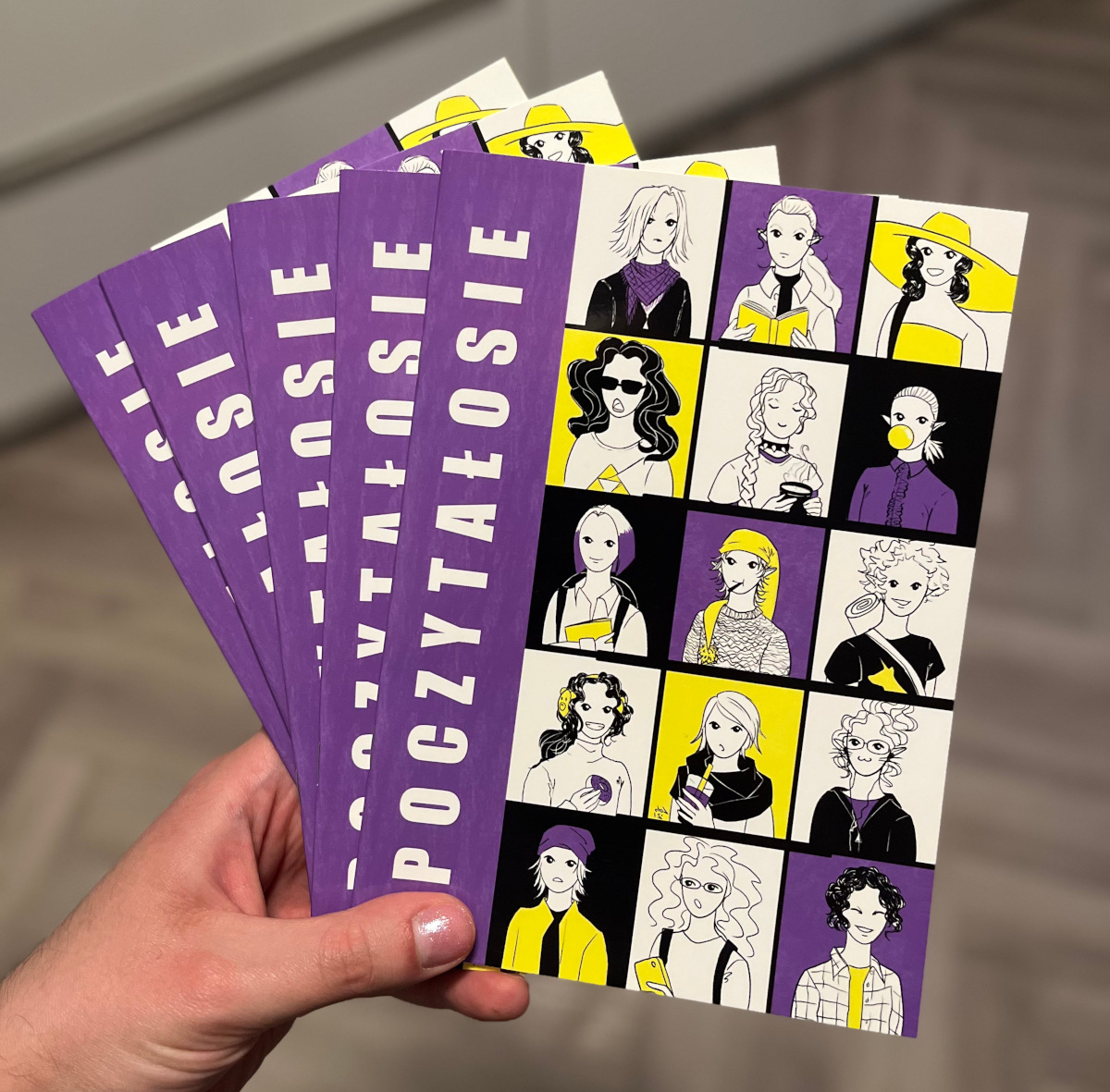 Picture of five copies of the zine. The cover is in the colours of the nonbinary flag, it's divided into rectangles, each with a drawn character; and on the left, vertically there's the title: “Poczytałosie”